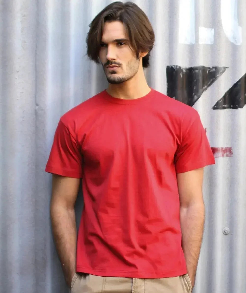 Uomo in t-shirt rossa streetwear davanti a muro industriale, stile urban casual