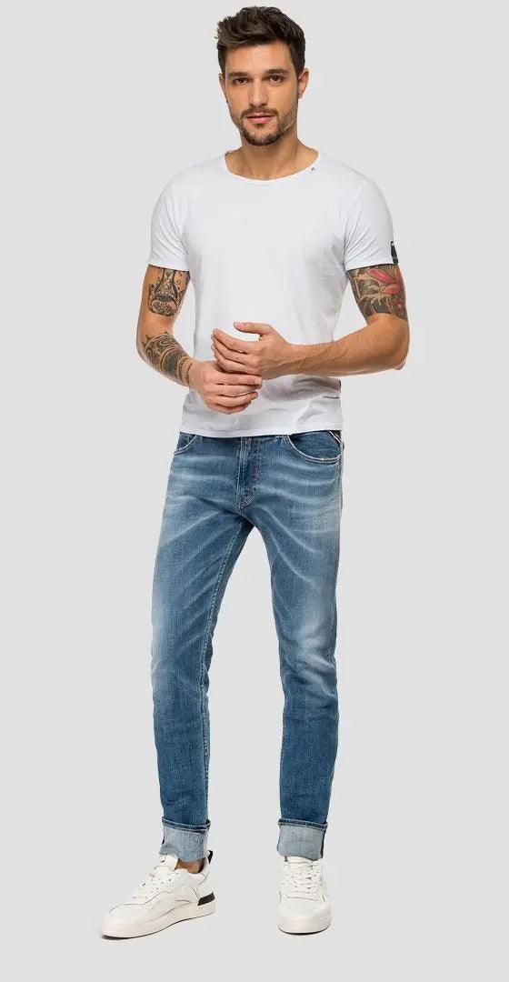 Uomo con tatuaggi indossa t-shirt bianca in cotone, jeans slim fit azzurri e sneakers bianche in stile streetwear urban